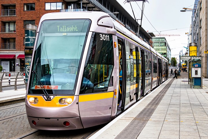 Modern tram in Tallaght, Dublin, stopped at platform on an urban street with people nearby.