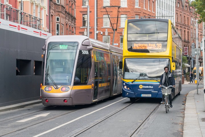 Tram, bus, and cyclist share a busy street in Dublin, showcasing urban transportation diversity and city life.